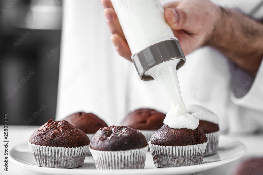 Male confectioner cooking tasty cupcakes in kitchen, closeup