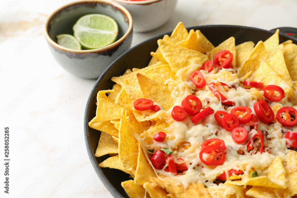 Frying pan with tasty nachos, cheese and chili on light table