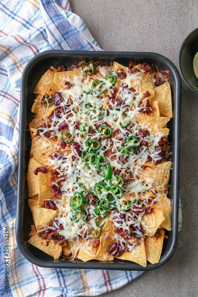 Baking dish with tasty nachos, minced meat, cheese and chili on grey table