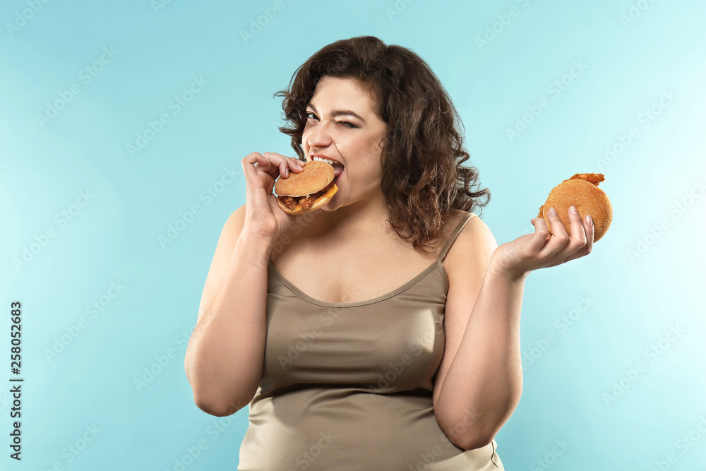 Overweight woman with burgers on color background