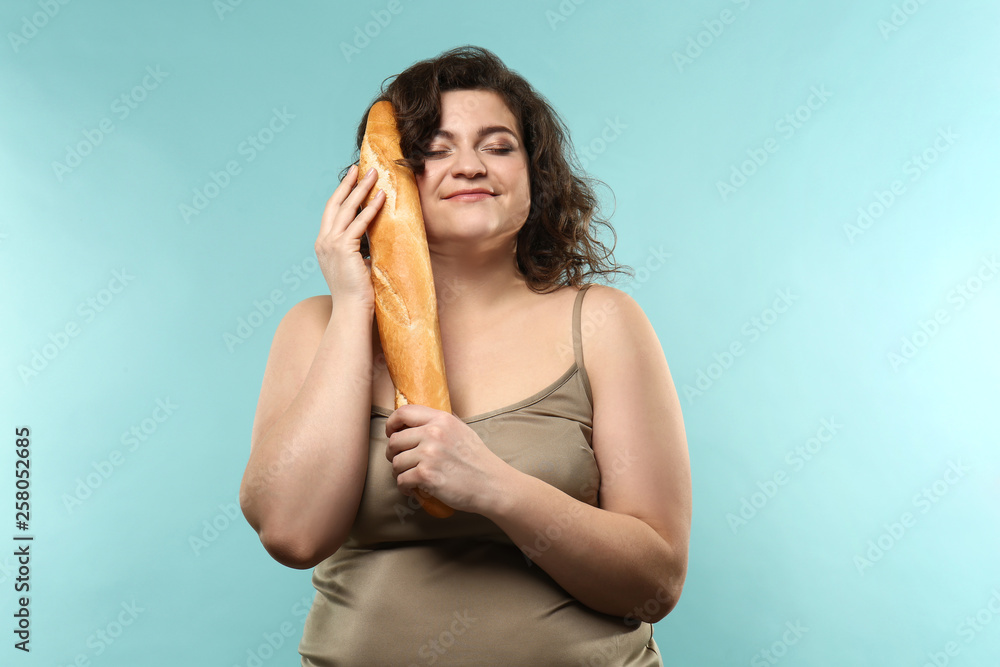 Overweight woman with baguette on color background