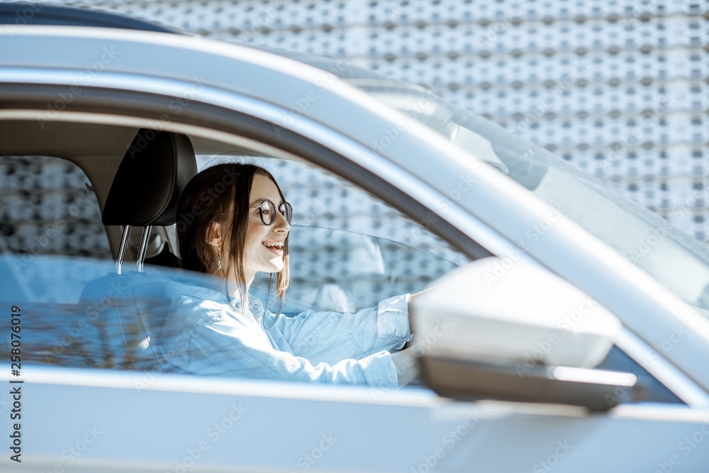 年轻快乐的女人在城市里开着豪车，从车窗看到的侧视图