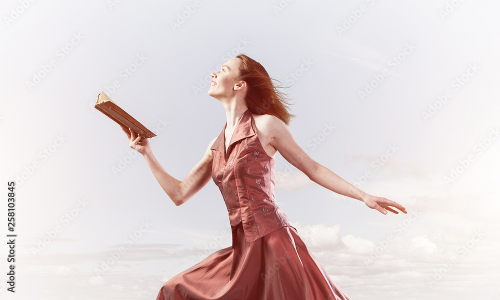 Girl against cloudy sky with opened book in palm as idea for knowledge