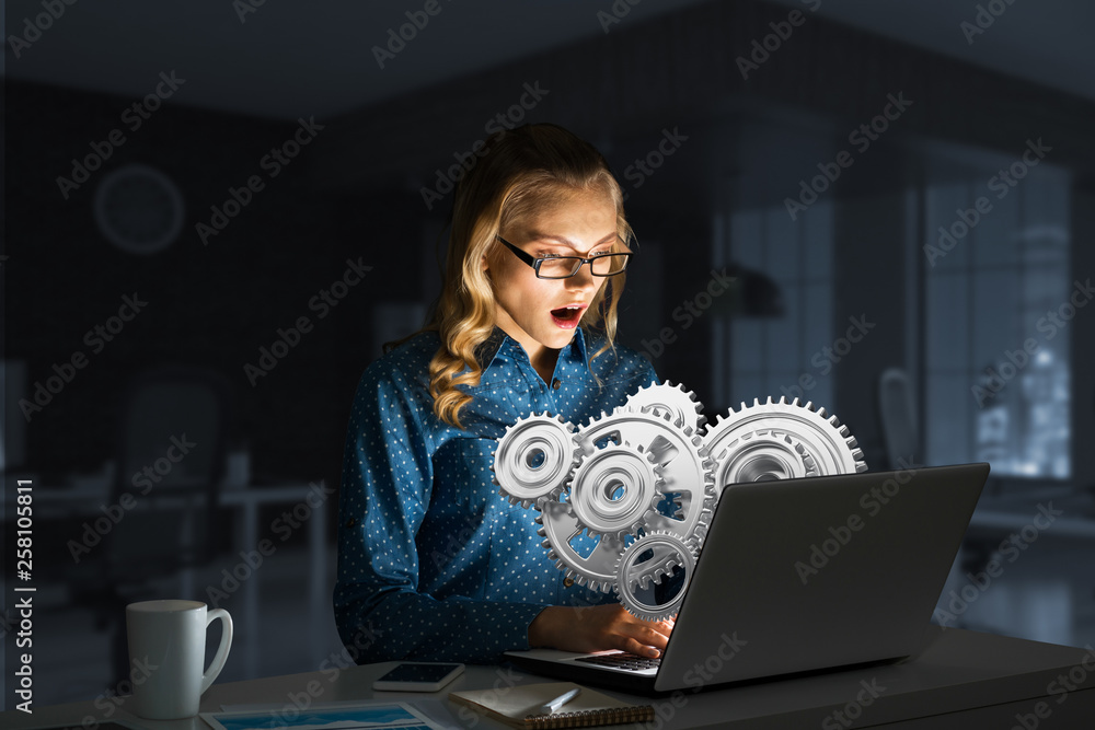 Attractive blonde wearing glasses in dark office using laptop. Mixed media