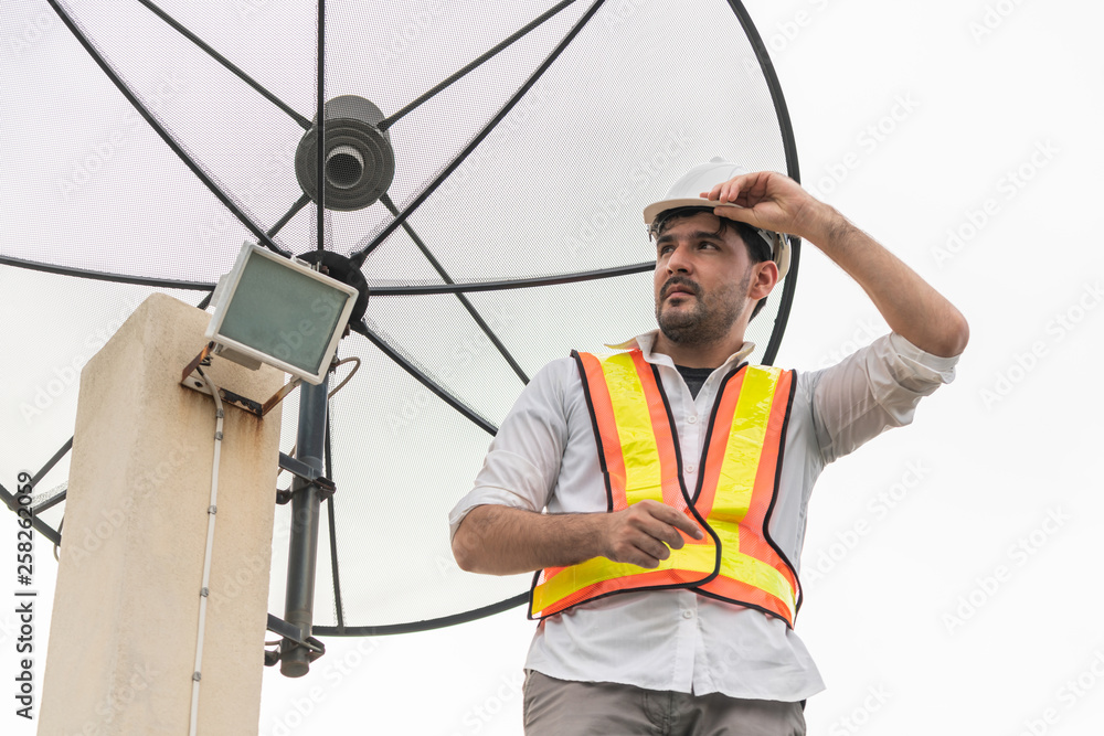 Professional technician or engineer standing on roof top of building working with satellite dish. Co