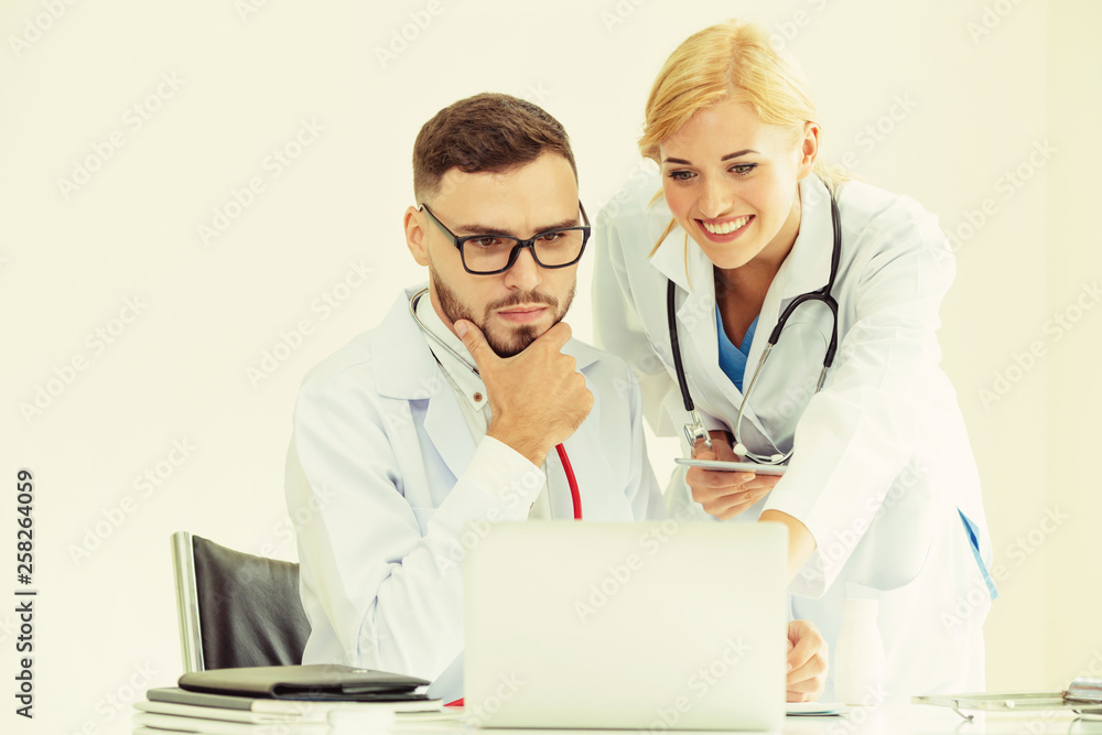 Doctor at hospital office working on laptop computer on the table with another doctor having discuss