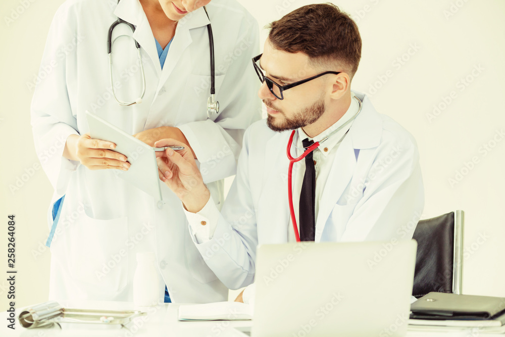 Doctor at hospital office working on laptop computer on the table with another doctor having discuss