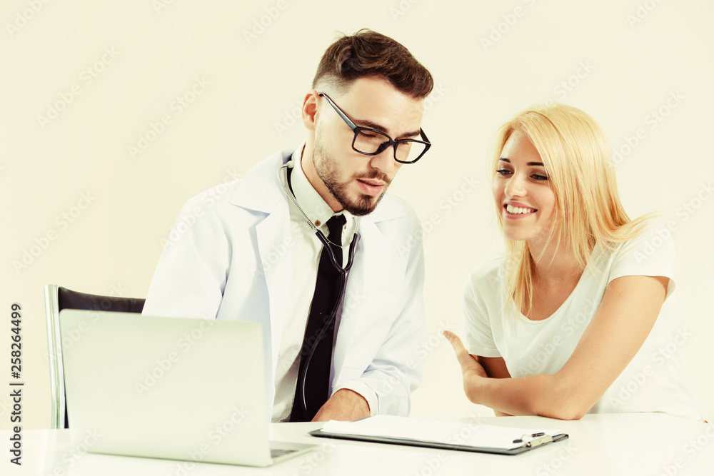 Male doctor talks to female patient in hospital office while looking at the patients health data on 