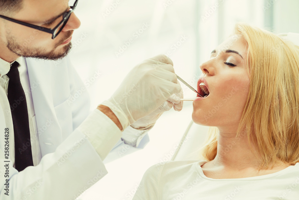 Young handsome dentist examining teeth of happy woman patient sitting on dentist chair in dental cli