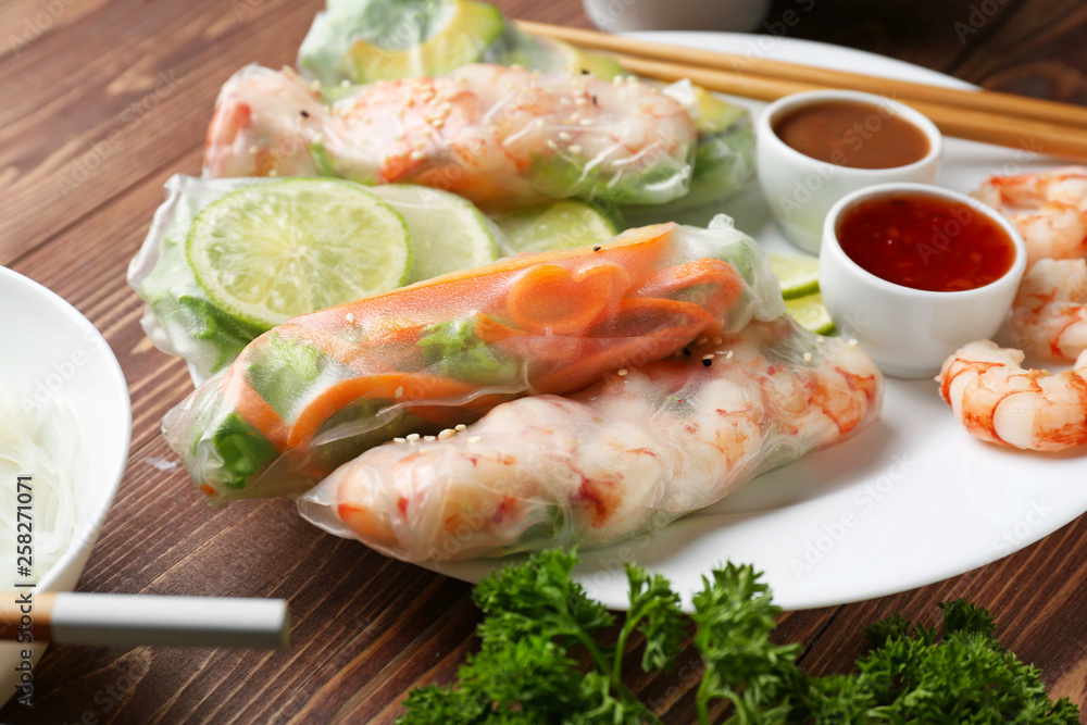 Plate with tasty spring rolls and sauces on wooden table