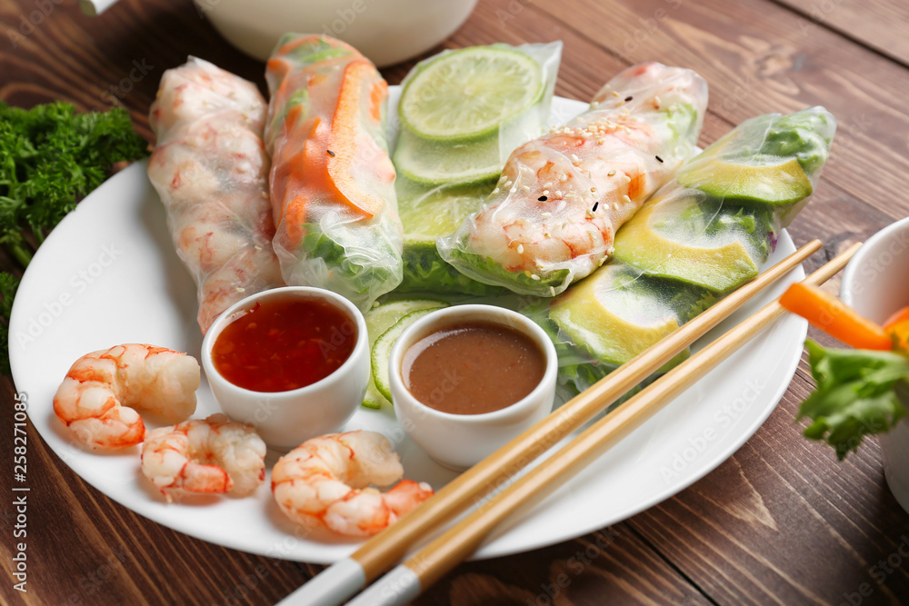 Plate with tasty spring rolls and sauces on wooden table