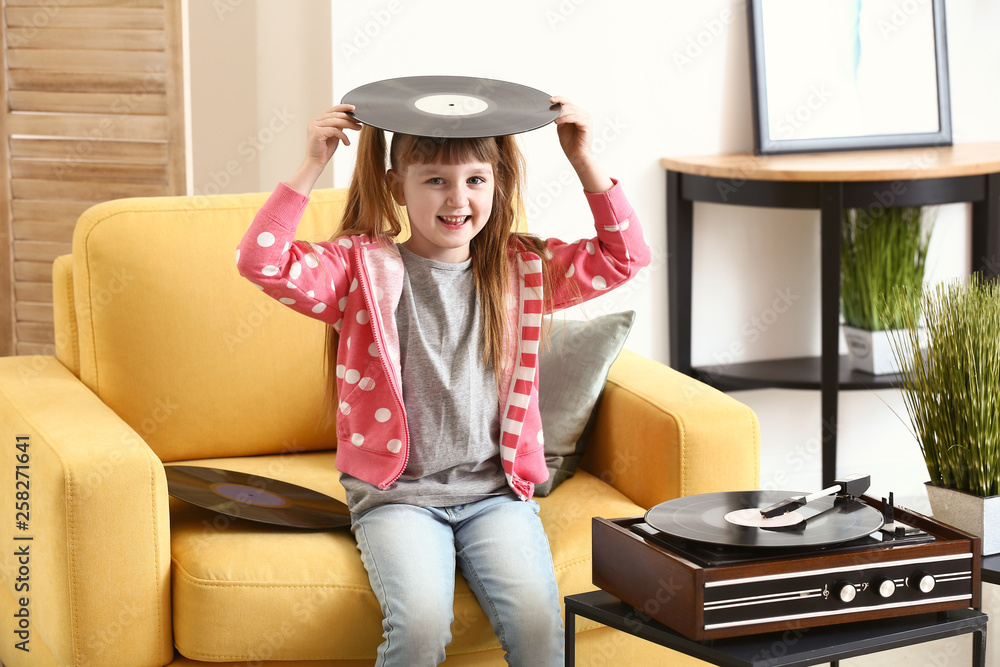 Cute little girl listening to music through record player at home