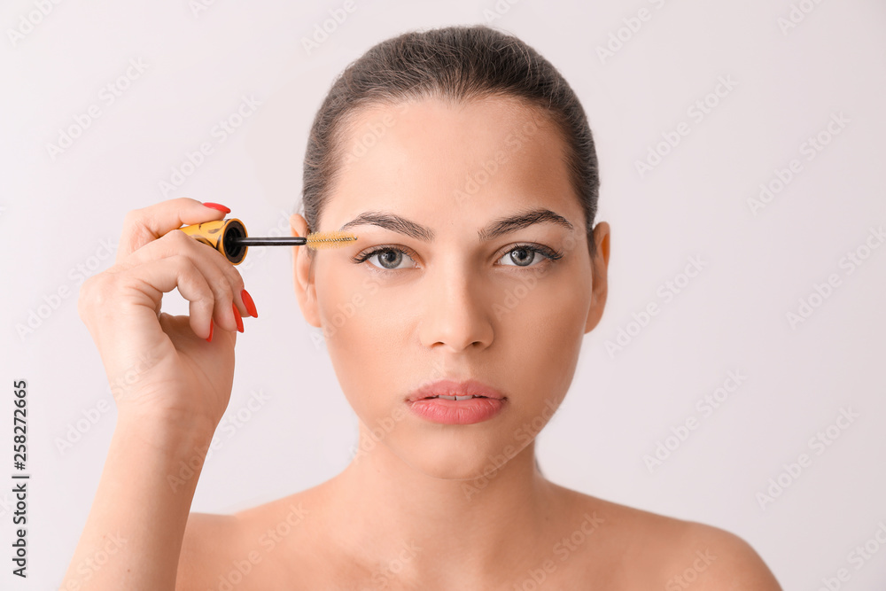 Beautiful young woman with eyelash extensions and special brush on light background