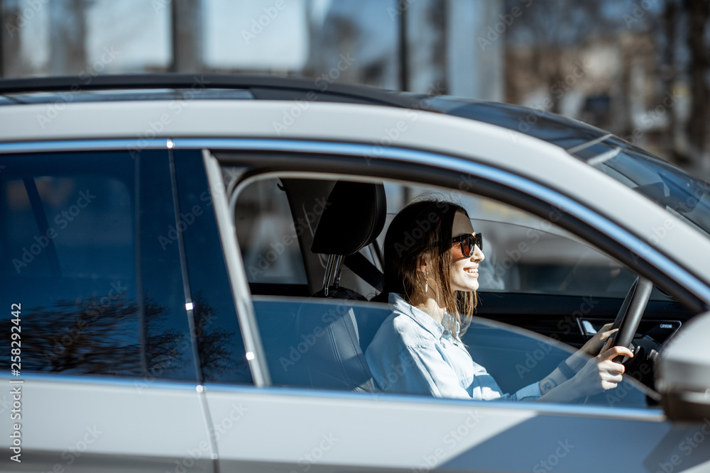 年轻快乐的女人在城市里开着豪车，从车窗看到的侧视图