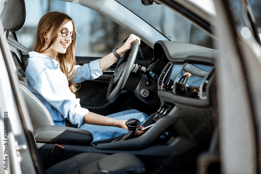 Young woman taking a smart phone from the place of wireless charging in the modern car in the city