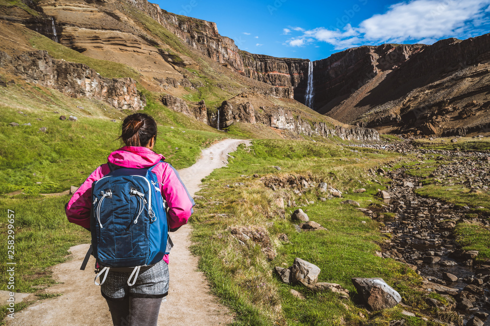 Woman traveler trekking in Icelandic summer landscape at the Hengifoss waterfall in Iceland. The wat