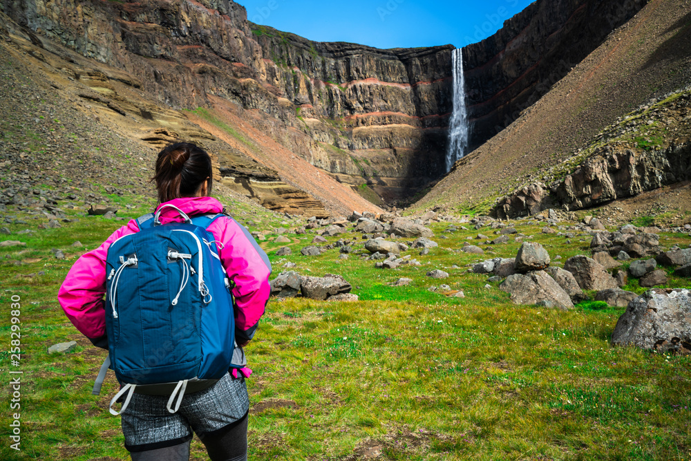 Woman traveler trekking in Icelandic summer landscape at the Hengifoss waterfall in Iceland. The wat