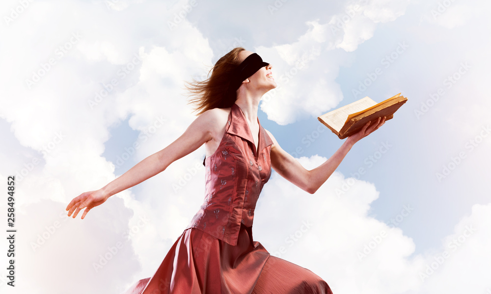 Girl against cloudy sky with opened book in palm as idea for knowledge