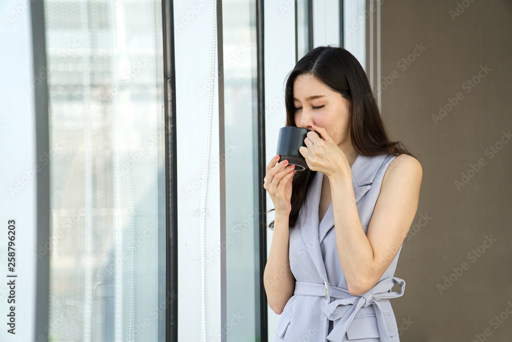 亚洲聪明漂亮的女孩站在窗户附近喝咖啡休息