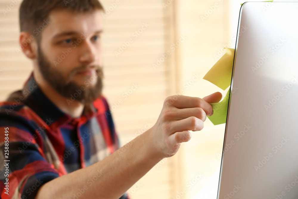 Male designer attaching stickers to monitor in office