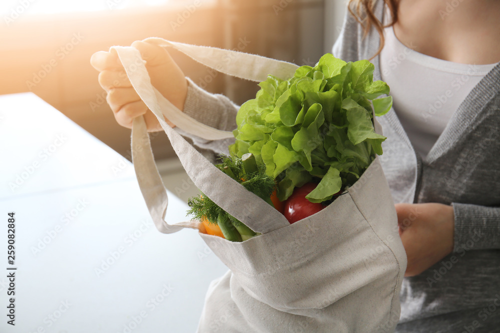 Young woman with fresh vegetables in eco bag indoors