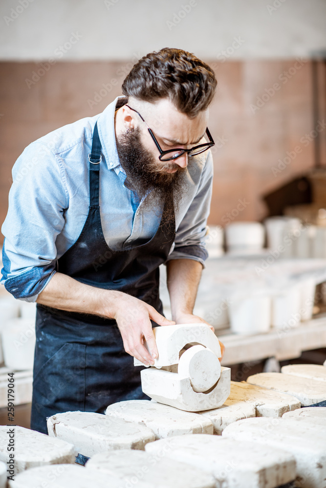 Handsome worker in apron getting clay products from the gypsum forms at the pottery manufacturing