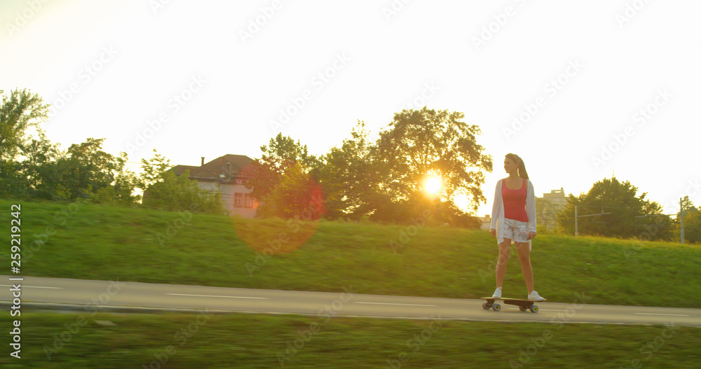 SUN FLARE: Carefree female skateboarder riding her e-longboard on sunny morning.