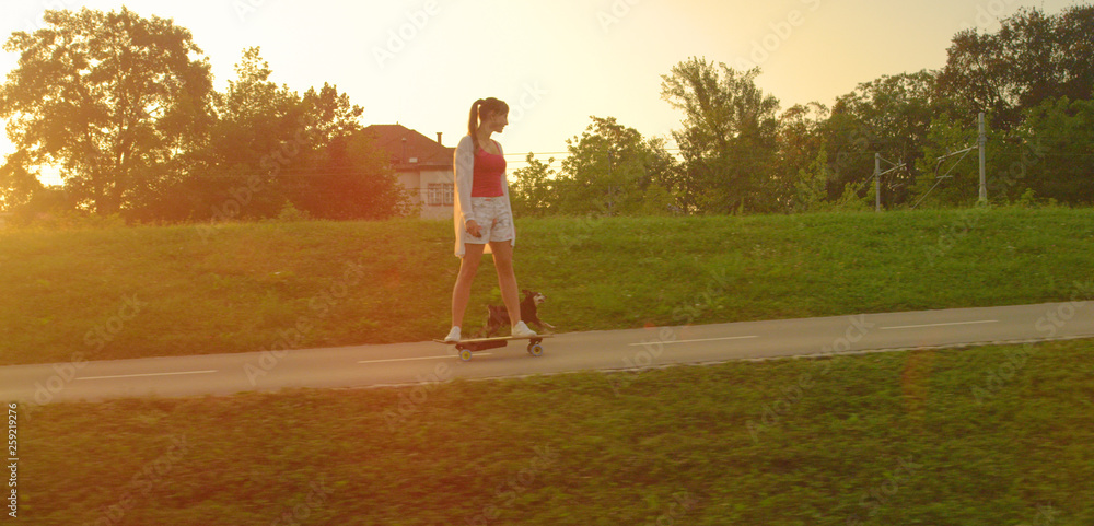 LENS FLARE: Happy little dog running next to girl riding an electric skateboard.