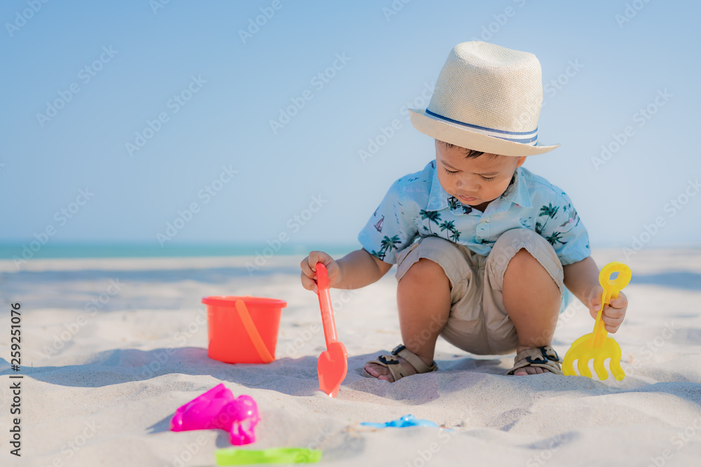 Asian two year old toddler boy playing with beach toys on beach.