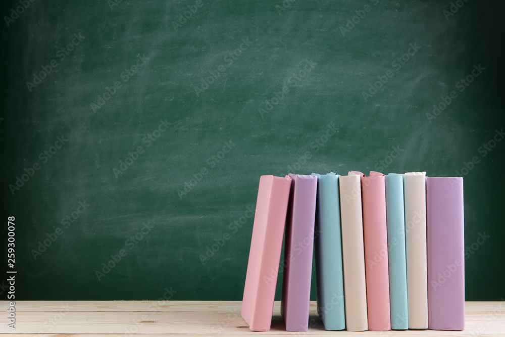 Education and reading concept - group of colorful books on the wooden table in the classroom, blackb