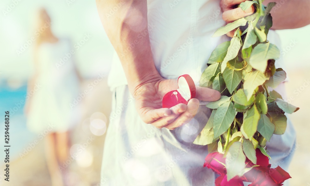 Man hiding bouquet of roses from woman at seaside