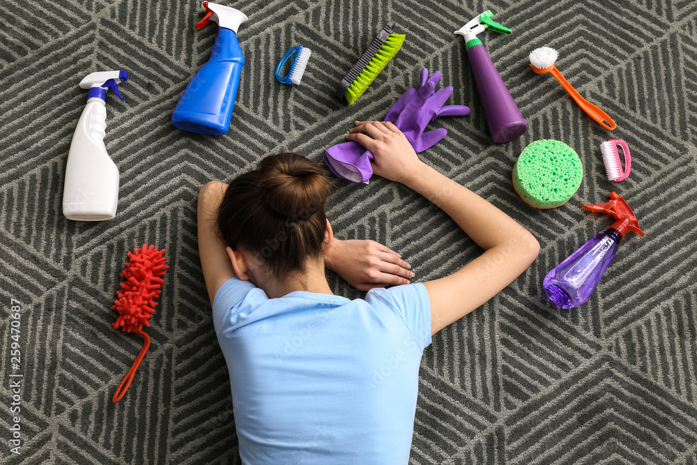 Tired woman with cleaning supplies lying on carpet