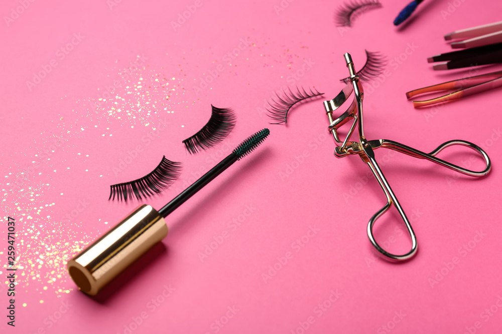 Mascara with false eyelashes and tools on color background