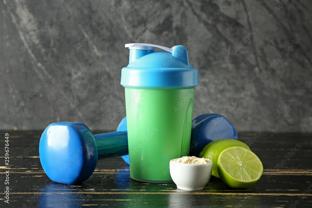 Bottle of protein shake with dumbbells on wooden table