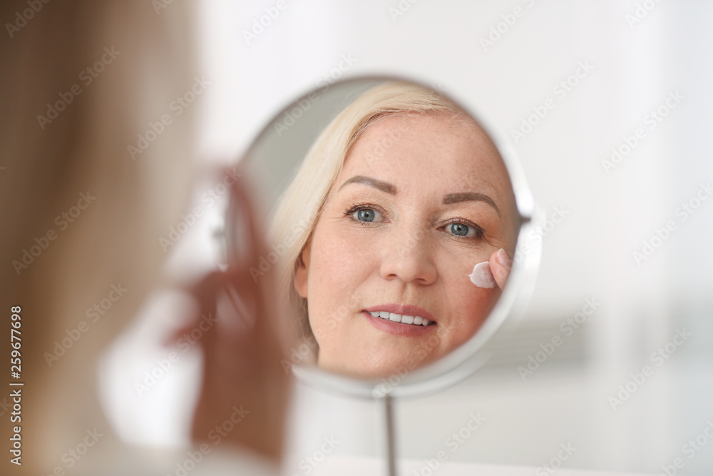 Mature woman applying facial cream at home