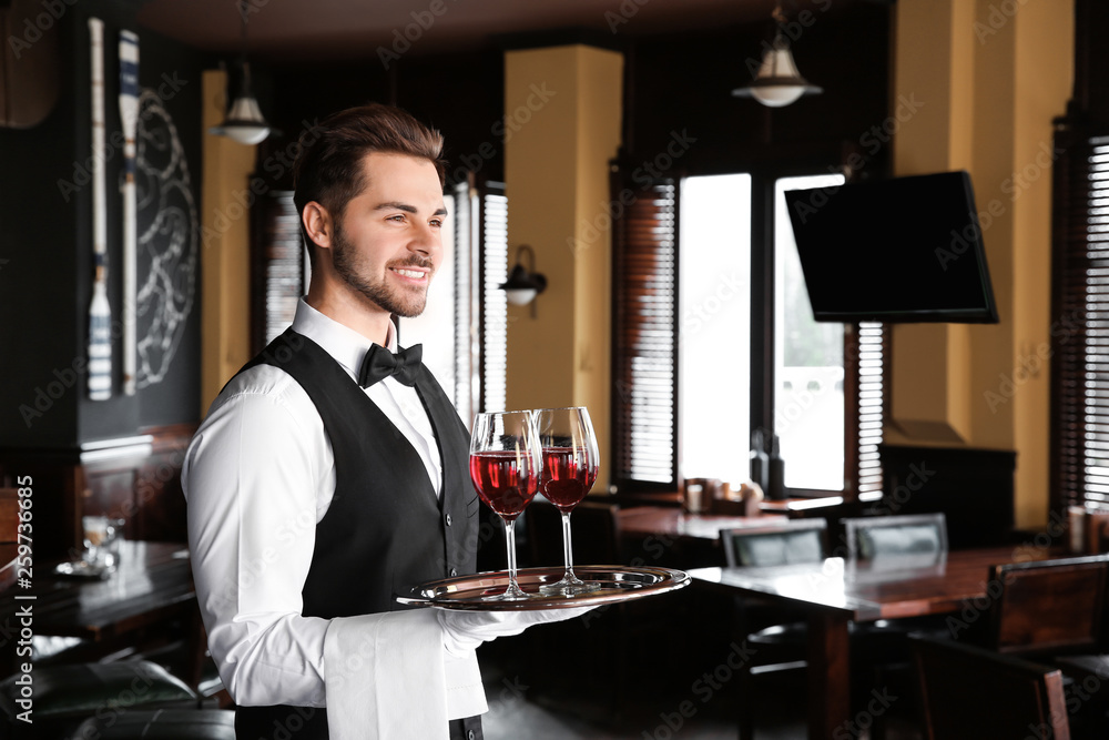 Young male waiter with glasses of wine in restaurant