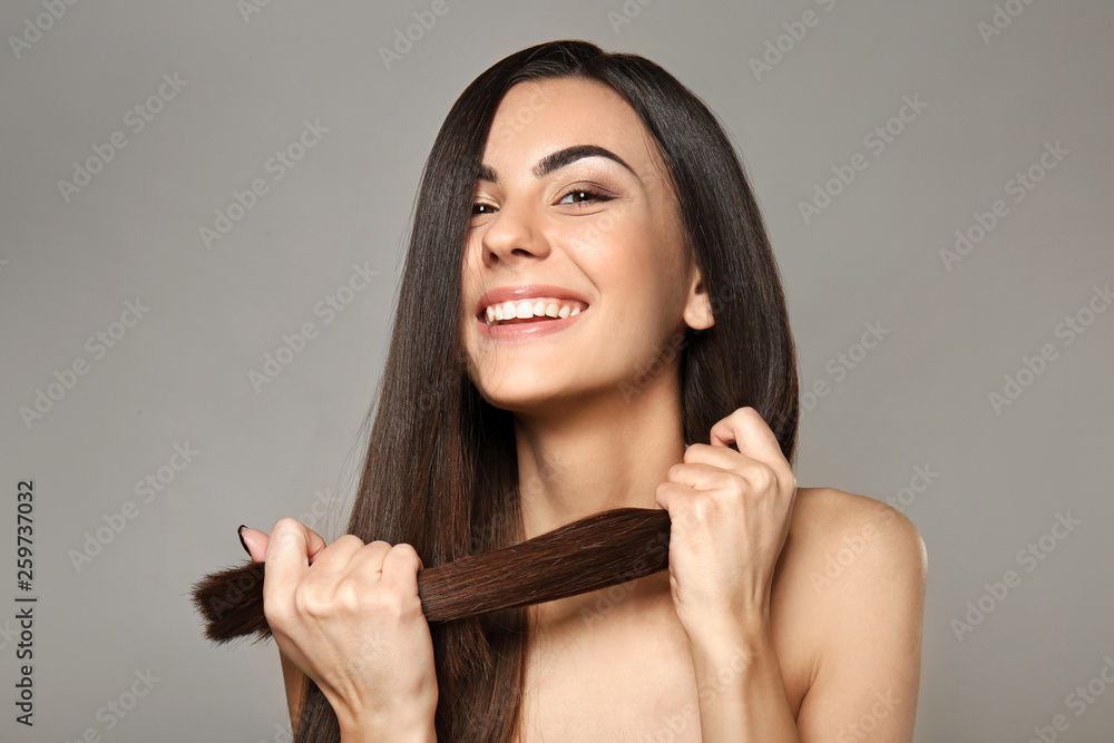 Portrait of beautiful young woman with healthy long hair on grey background