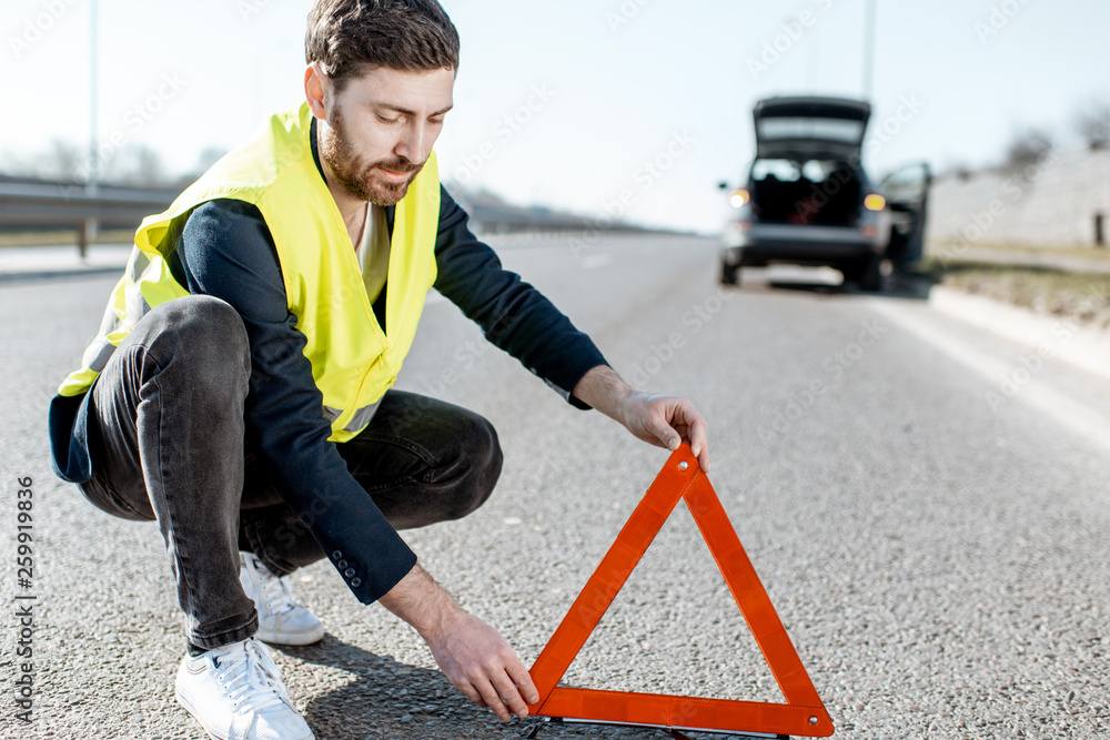 身穿路背心的男子在高速公路上放置紧急三角标志，背景是破碎的汽车