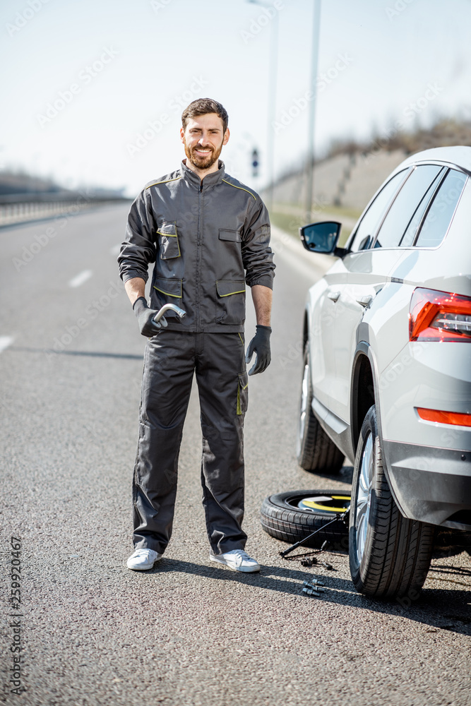 高速公路上，一位穿着制服的英俊道路救援人员站在破碎的汽车附近的画像