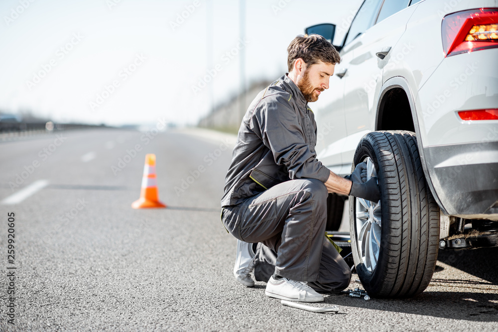 穿着制服的英俊道路救援人员在高速公路上更换车轮