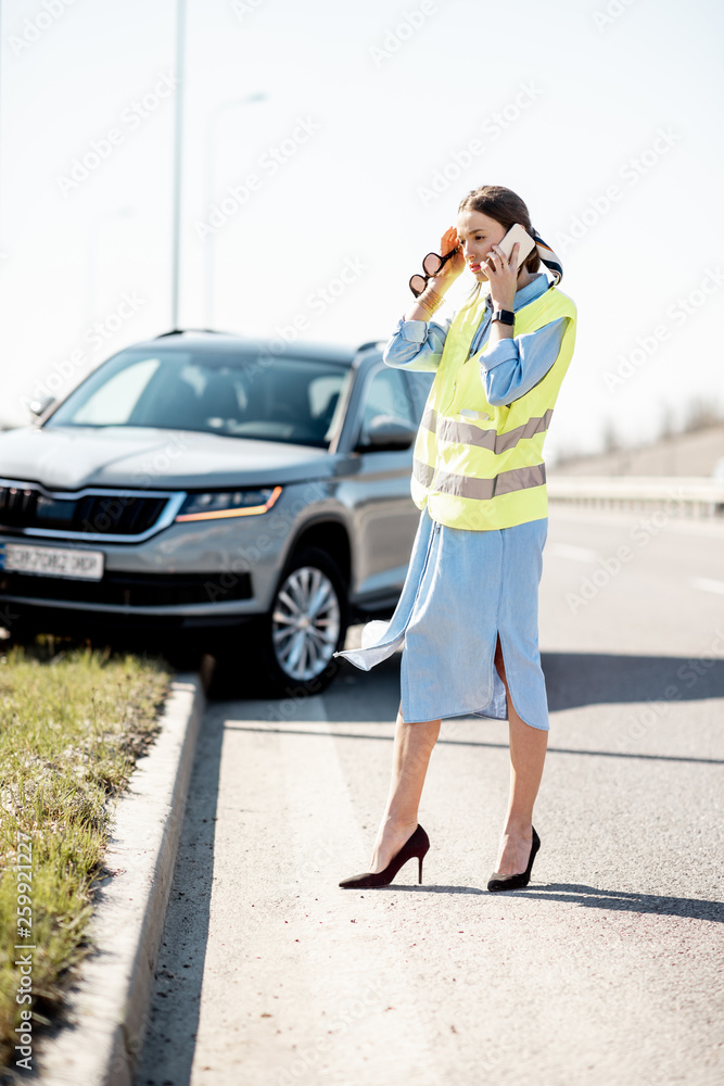 Embarrassed woman calling road assistance standing near the car during the road accident on the high