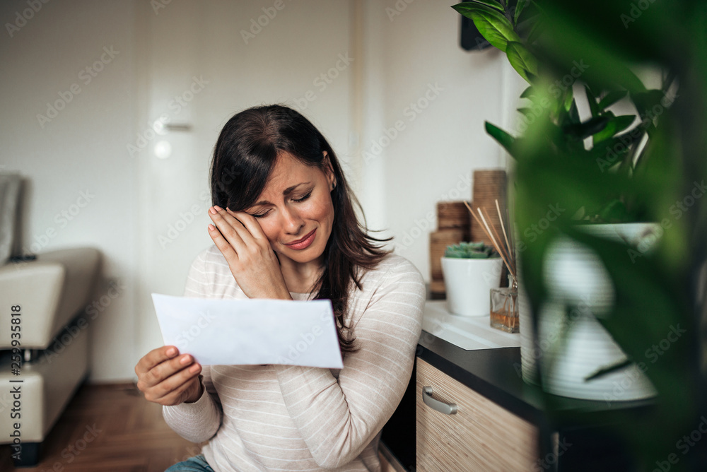 Portrait of a sad woman broken after reading bad news in a letter at home.