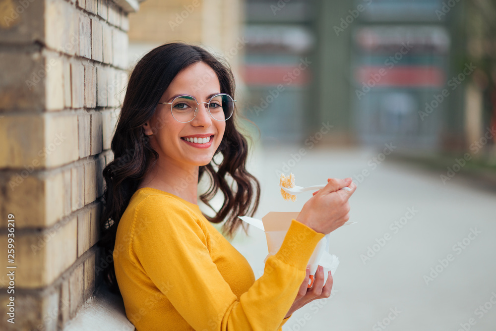 Portrait of a positive casual young woman eating take-away food on a break, looking at camera.