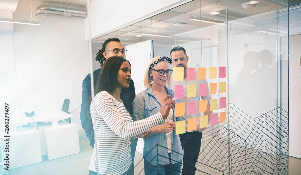 Smiling work colleagues brainstorming with notes on a glass wall