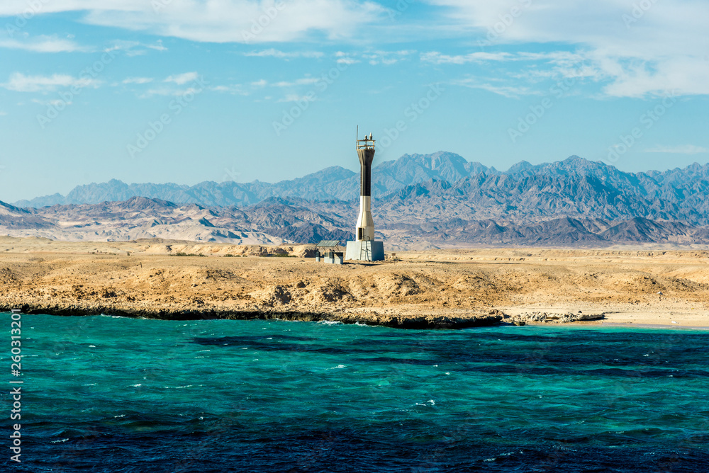 Seascape, high lighthouse against the blue sea with high bald mountains in the background