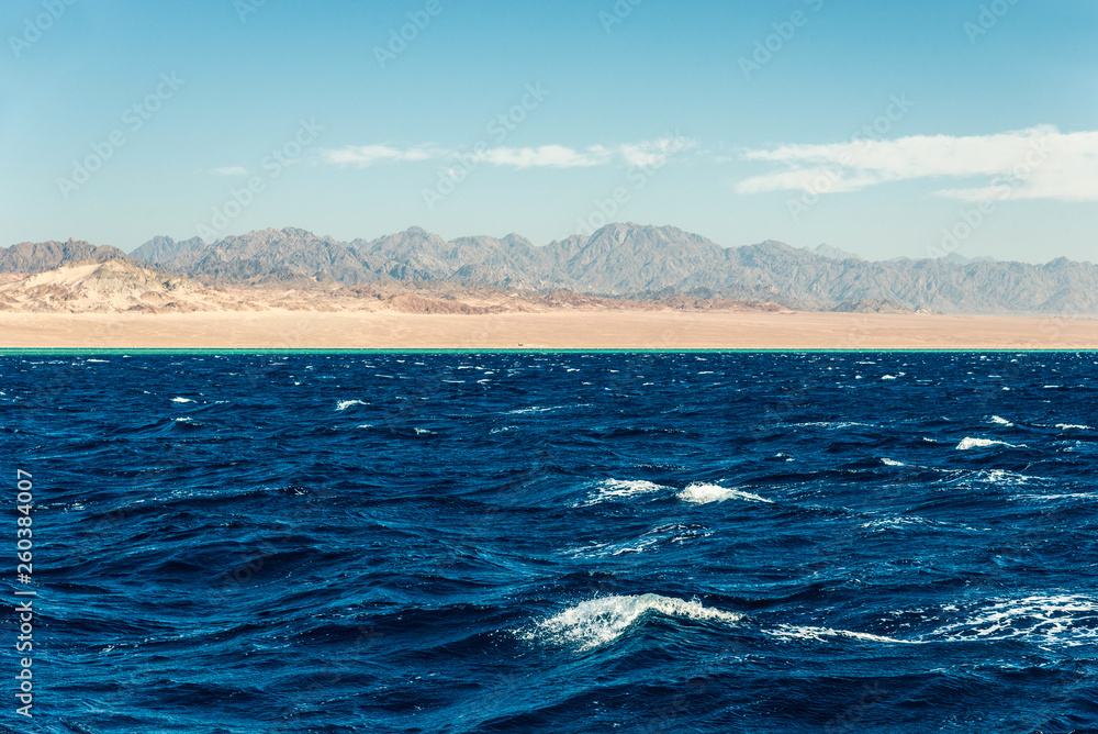 Seascape, view of the blue sea with high bald mountains in the background