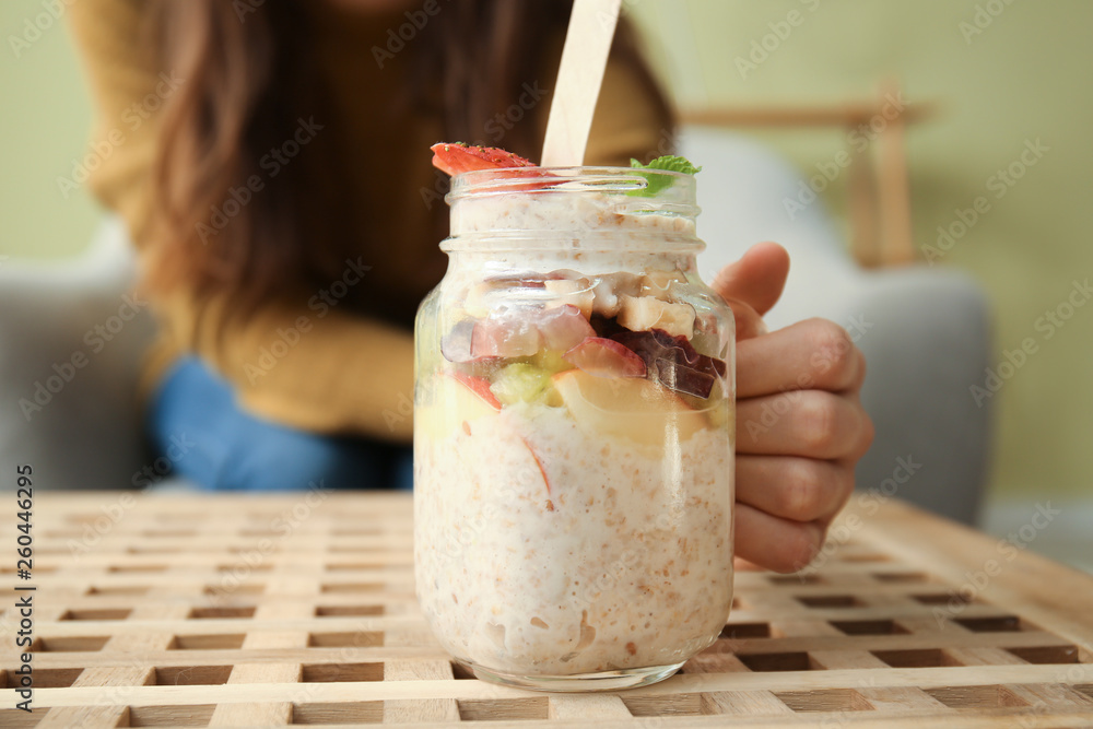 Young woman with tasty sweet oatmeal in jar on table