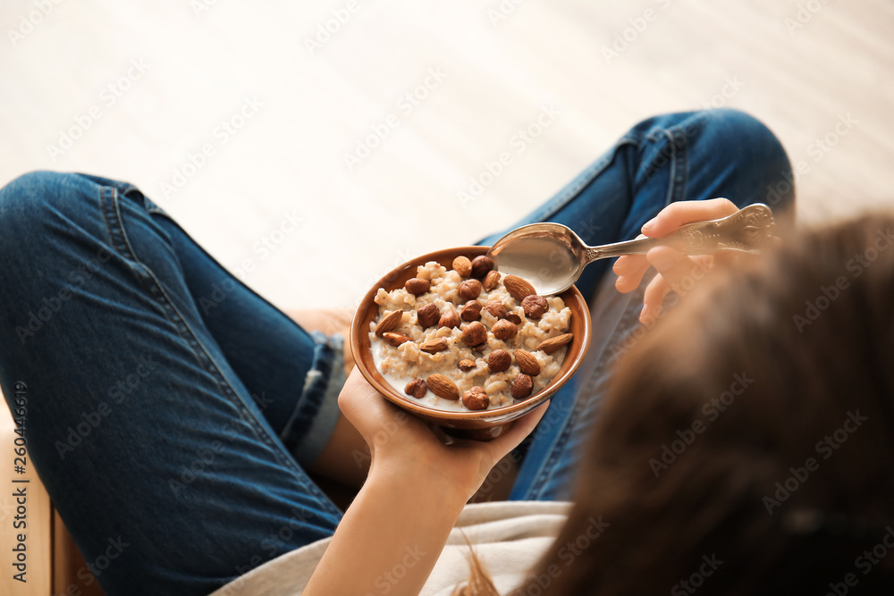 Young woman eating tasty sweet oatmeal at home