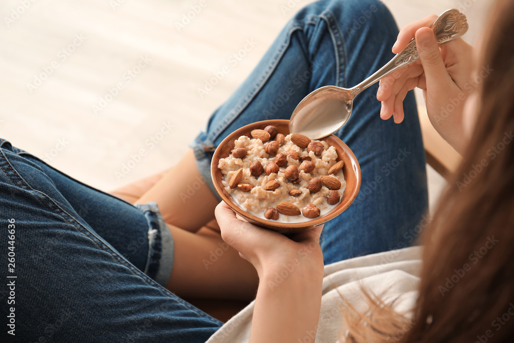 Young woman eating tasty sweet oatmeal at home