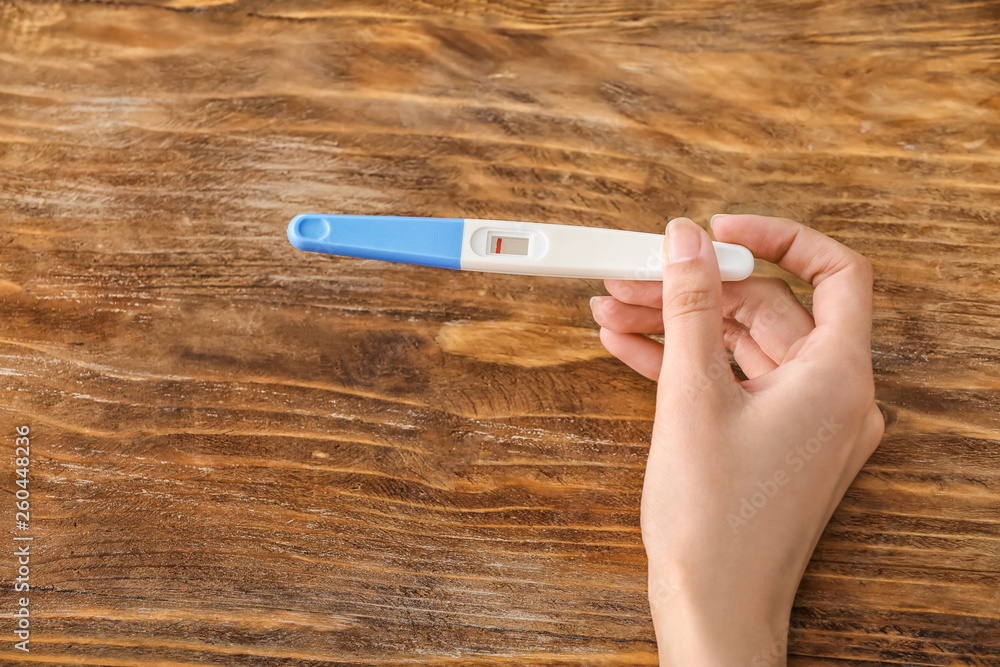 Female hand with pregnancy test on wooden background